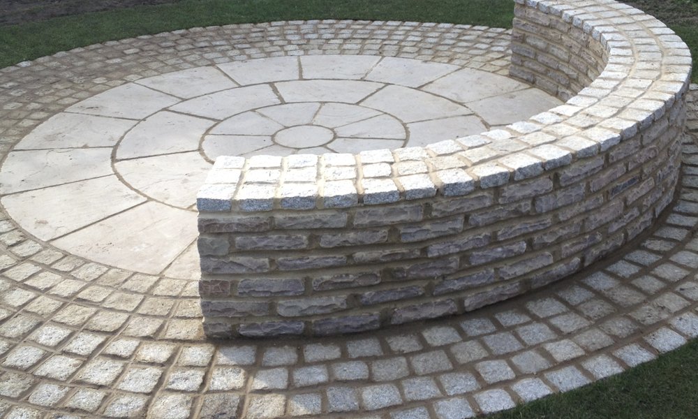 Sandstone circle feature with a curved granite sett retaining wall, built by Ideal Landscapes
